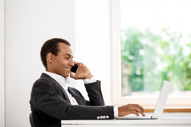 Young successful businessman speaking on phone, typing laptop