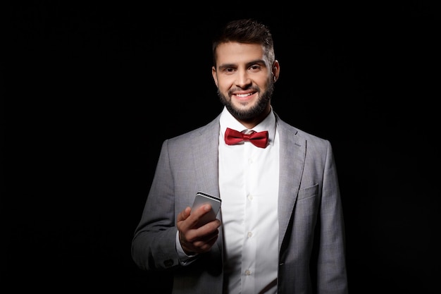 Young successful businessman in suit holding phone smiling on black
