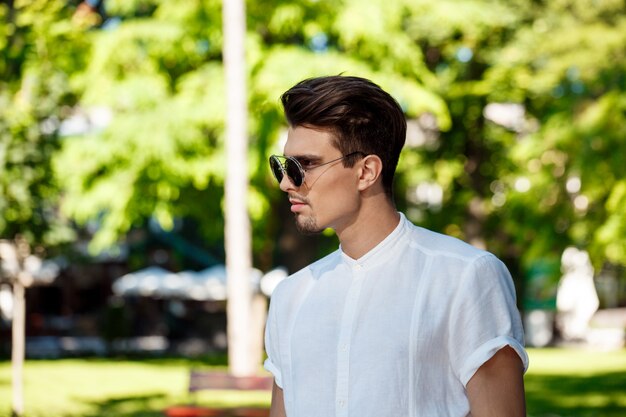 Young successful businessman in sunglasses walking around sunny city