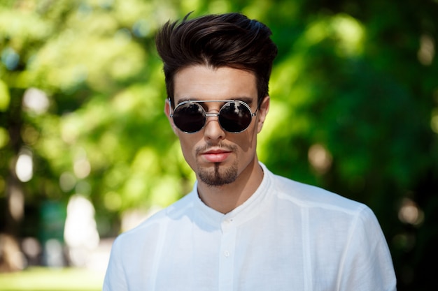 Young successful businessman in sunglasses walking around sunny city