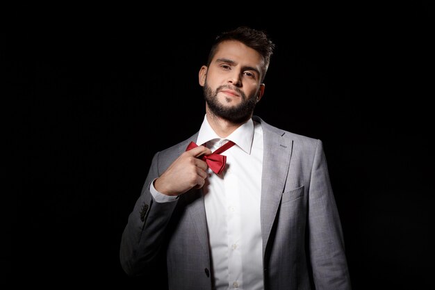 Young successful businessman taking off bowtie over black wall