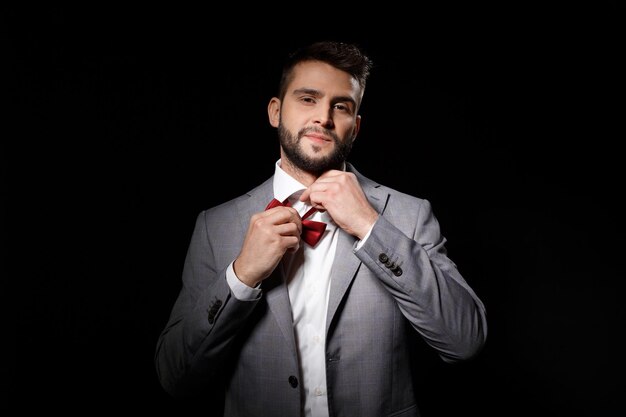 Young successful businessman taking off butterfly over black background