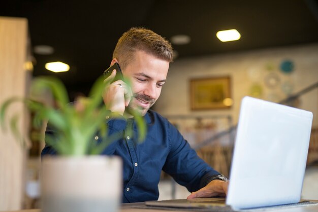 Young successful businessman talking on the phone and using laptop at cafe bar restaurant