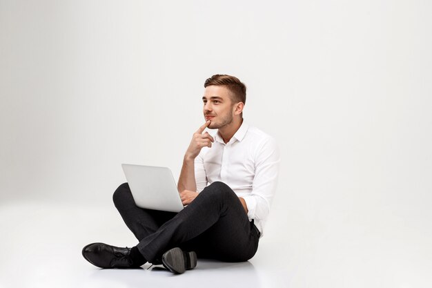 Молодой успешный бизнесмен мышления, сидя с ноутбуком.