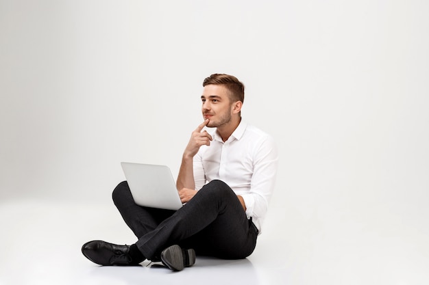Young successful businessman thinking, sitting with laptop.