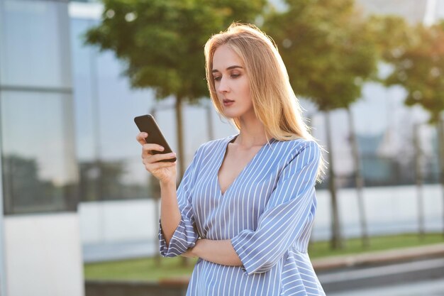 Молодая успешная деловая женщина ждет своего нового партнера на улице с мобильным телефоном в руках.