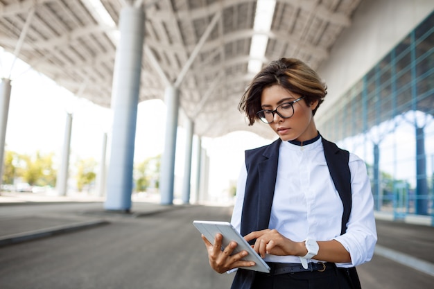 Free photo young successful businesswoman looking at tablet, standing near business centre.