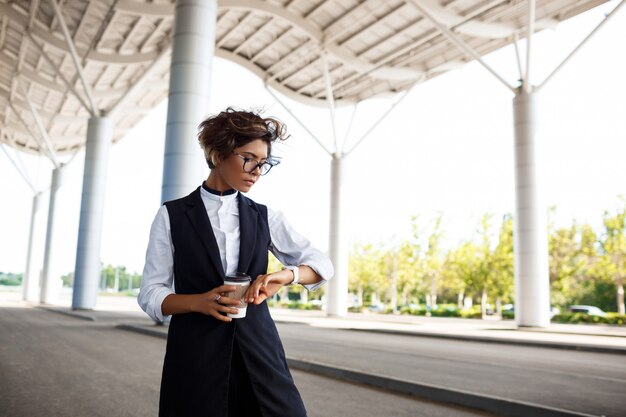 Young successful businesswoman looking at watch, standing near business centre.