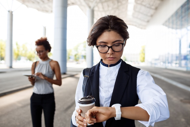 Young successful businesswoman looking at watch, standing near business centre.