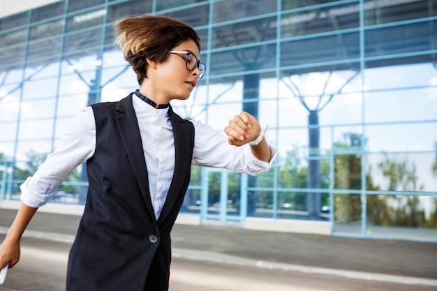 Young successful businesswoman running looking at watch over business centre