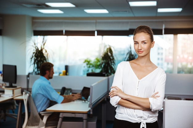 Young successful businesswoman smiling, posing with crossed arms, over office