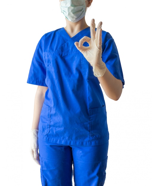 파란색 의료 제복을 입은 젊은 성공적인 여성 의사와 괜찮아 기호를 표시하는 마스크
