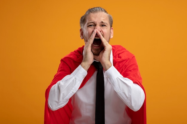 Young superhero guy wearing tie looking at camera calling someone isolated on orange background