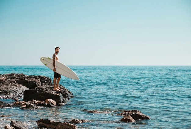 Young surfer standing on rocky shore