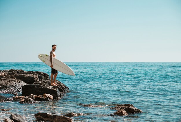 Young surfer standing on rocky shore