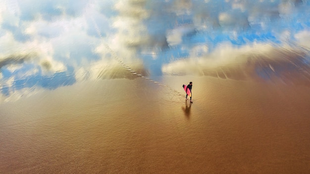 Молодой серфер гуляет по песчаному пляжу