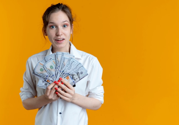 Молодая удивленная русская блондинка держит деньги на апельсине с копией пространства