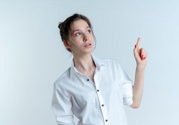 Young surprised blonde russian girl looks and points at side isolated on white space with copy space