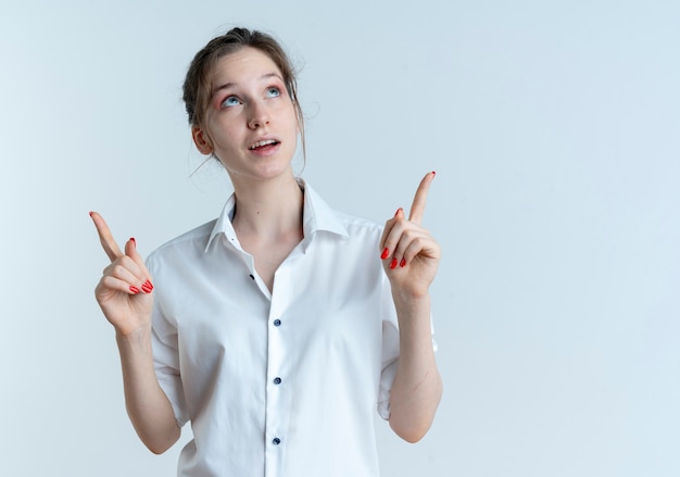 Young surprised blonde russian girl looks and points up isolated on white space with copy space