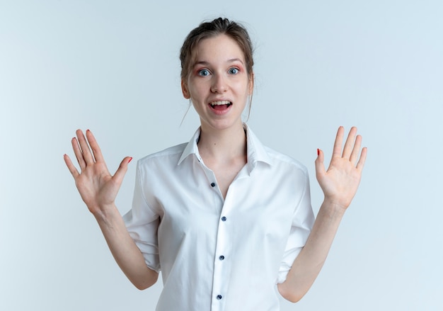 Young surprised blonde russian girl stands with raised hands isolated on white space with copy space