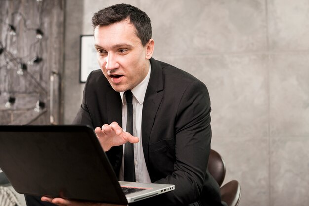 Young surprised businessman browsing laptop at home