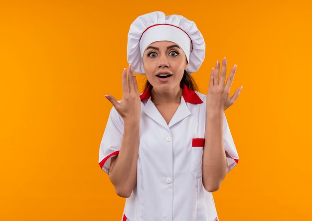 요리사 유니폼에 젊은 놀된 백인 요리사 소녀 복사 공간이 오렌지 벽에 고립 된 손을 보유