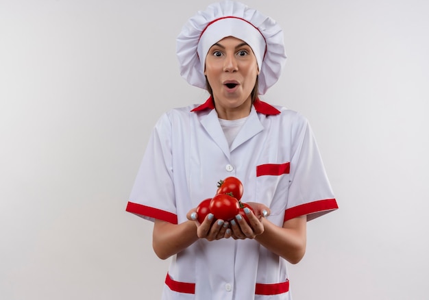 Free photo young surprised caucasian cook girl in chef uniform holds tomatoes in hands on white  with copy space