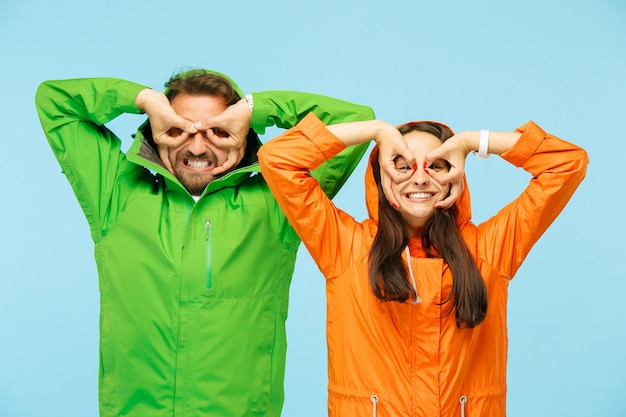 The young surprised couple at studio in autumn jackets isolated on blue.