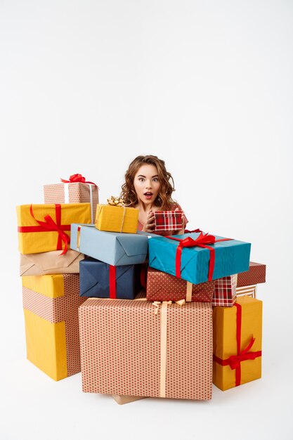 Young surprised curly woman among gift boxes