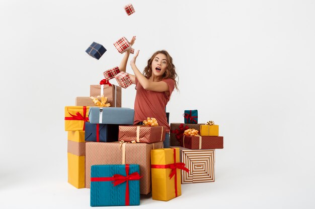 Young surprised curly woman among lying and falling gift boxes