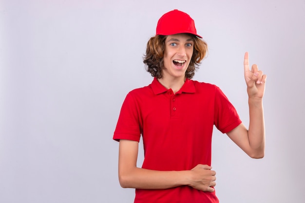 Giovane uomo di consegna sorpreso in uniforme rossa rivolta verso l'alto una grande idea sorridente con la faccia felice su sfondo isolato