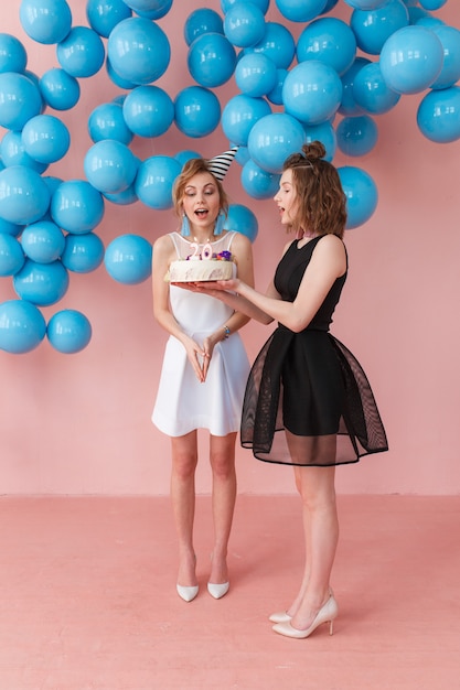 Young surprised girl holding a birthday cake and her friend standing close. 