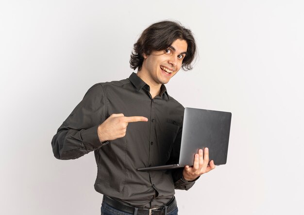 Young surprised handsome caucasian man holds and points at laptop isolated on white background with copy space