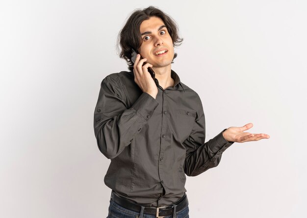 Young surprised handsome caucasian man talks on phone and points at side isolated on white background with copy space