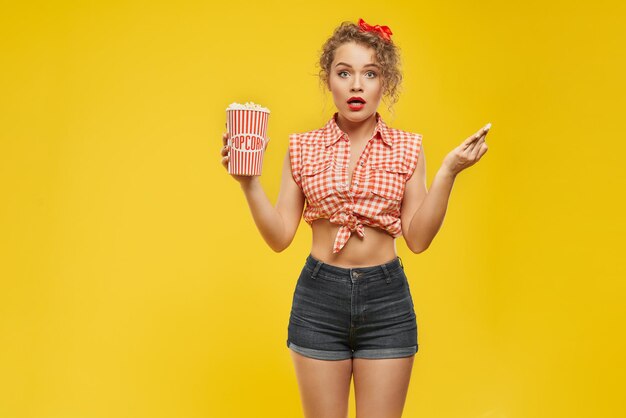 Young surprised pretty girl with popcorn posing at camera