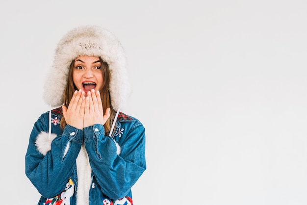 Young surprised woman in fur hat with hands near chin 