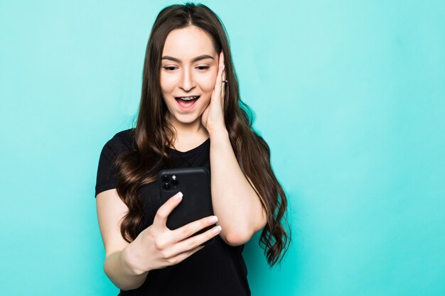 Young surprised woman with phone isolated on turquoise wall