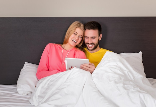 Young Sweet Couple on Bed Watching Something on Tablet Gadget. Concept about technology and people