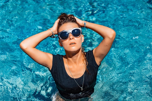 молодая загорелая женщина в солнечных очках в бассейне, мода, брызги.
