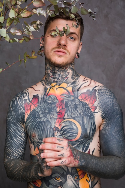 Молодой татуированный мужчина с пирсингом в носу и ушах смотрит в камеру