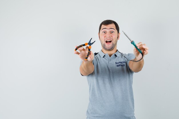 Young technician in grey uniform holding paint roller and looking cheerful , front view.