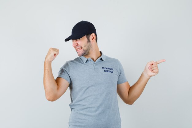 Young technician in grey uniform pointing to the right side and looking happy.