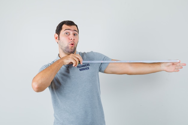 Free photo young technician in grey uniform using tape measure and looking surprised.