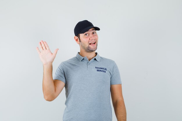 Young technician in grey uniform waving hand for greeting and looking jolly.