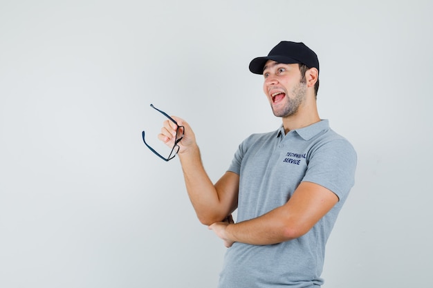 Young technician holding glasses in grey uniform and looking optimistic.