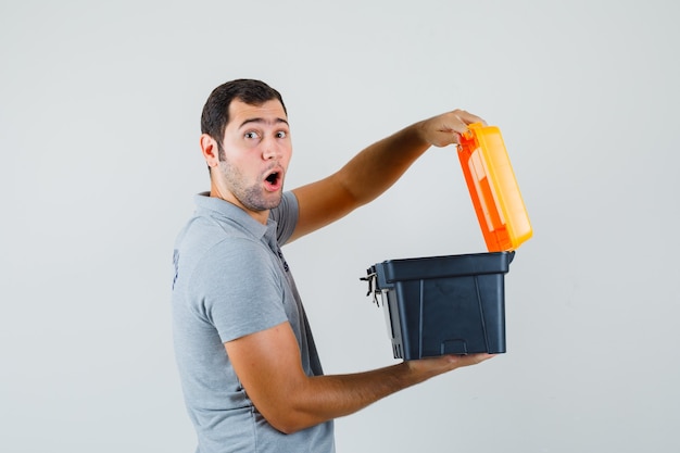 Free photo young technician holding opened toolbox in grey uniform and looking dazed.