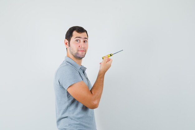 Young technician holding screwdriver and posing in grey uniform and looking focused.