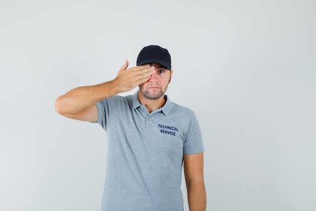 Young technician keeping hand on eye in grey uniform and looking calm.