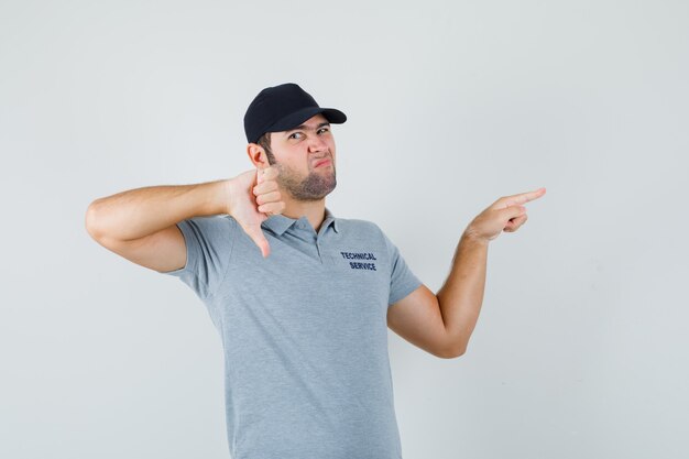 Young technician pointing aside, showing thumb down in grey uniform and looking gloomy.