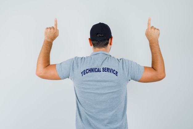 Free photo young technician pointing up in grey uniform and looking confident, back view.